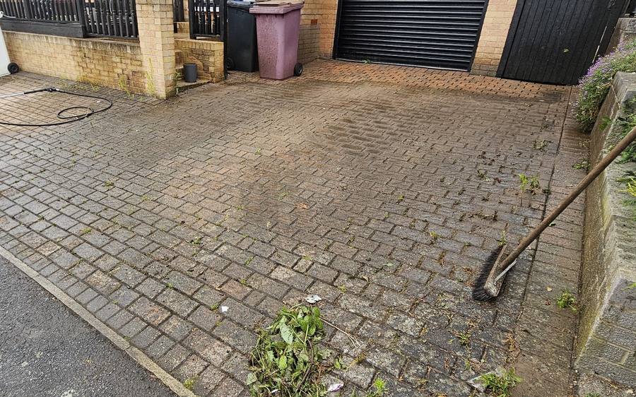 A block paving driveway dulled with dirt and weeds through the joints